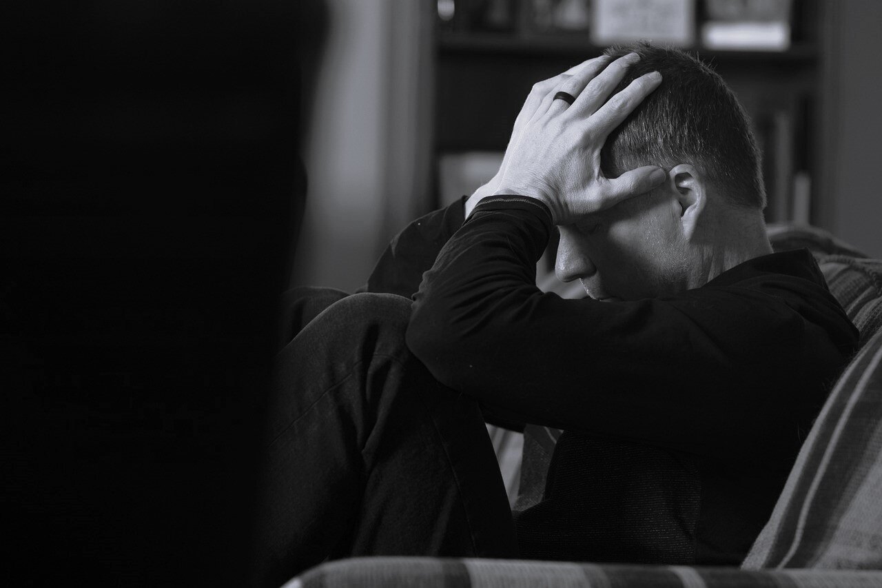 A man with mental health issues sits holding hid head in his hands